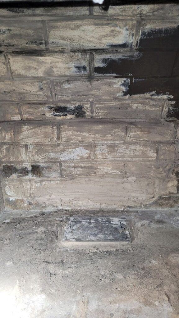 A brick fireplace interior with visible soot and a metal ash cleanout hatch.