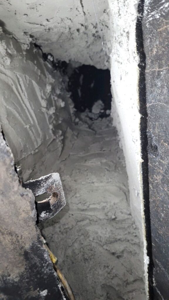 Interior view of a dirty air duct showing accumulation of dust and possible wear
