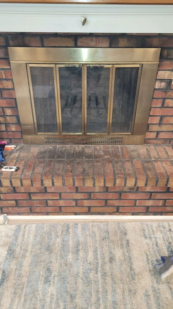 Brick fireplace with a brass screen and tools on the hearth