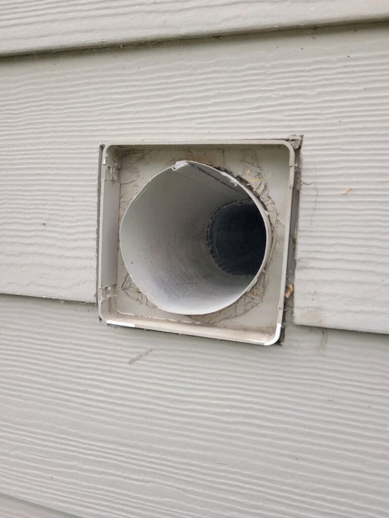 Close-up of an exterior dryer vent with a slightly open flap on house siding.