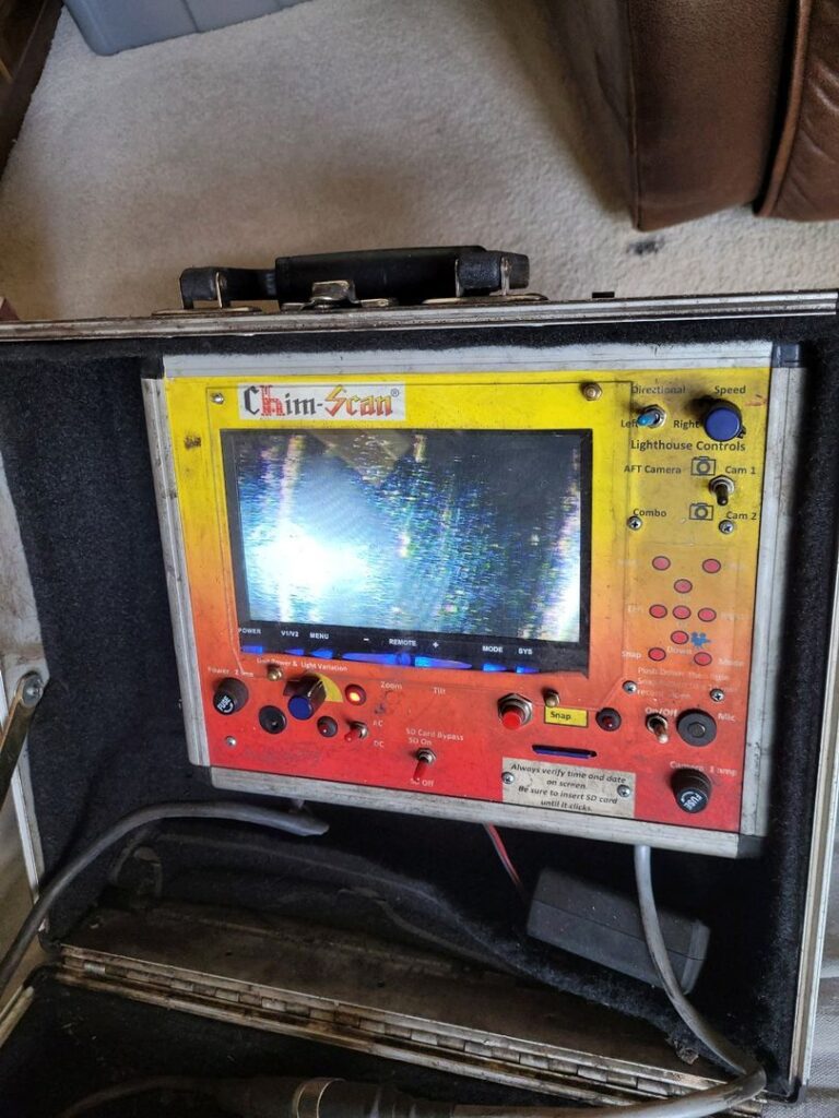 A Chim-Scan inspection device with various control buttons and a blurred screen image, used for examining the inside of chimneys.