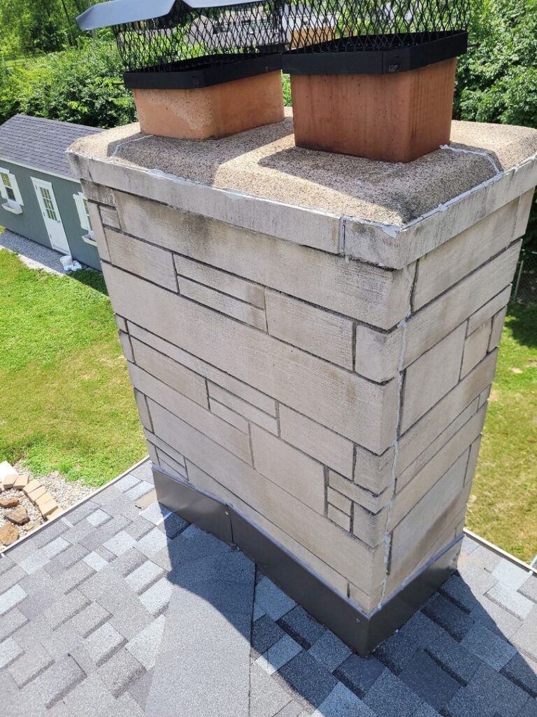 Dual-flue chimney with metal caps on a house roof during a sunny day.