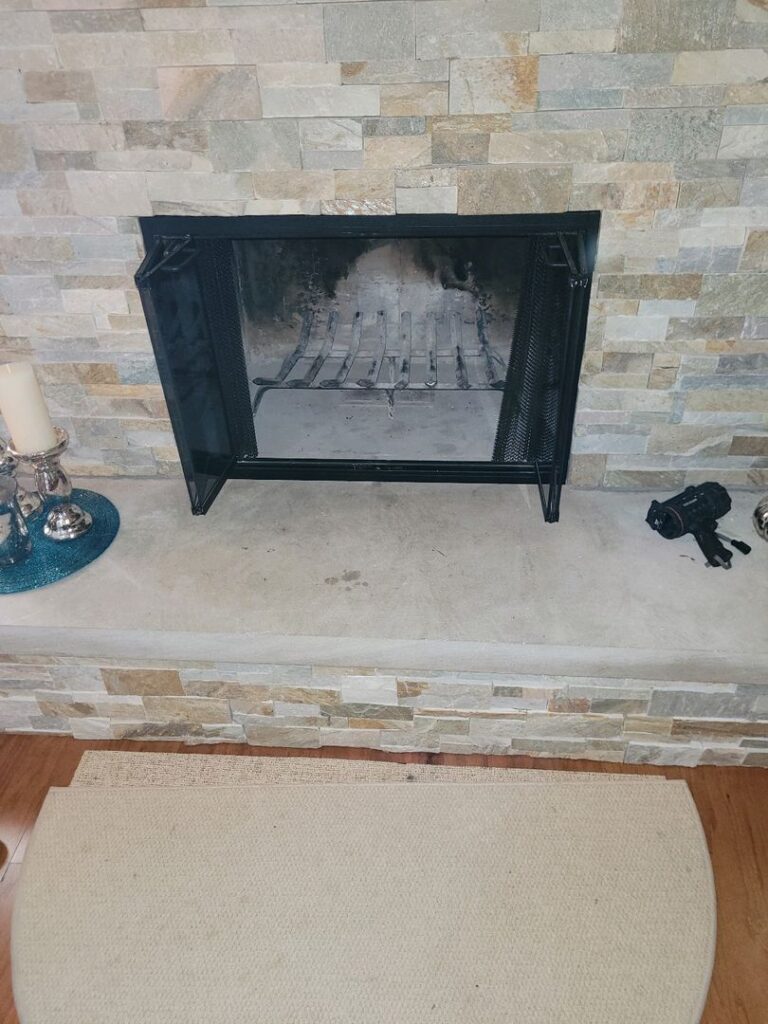 A clean and tidy fireplace area with stone tiles, ash inside the fireplace, and decorative items nearby.