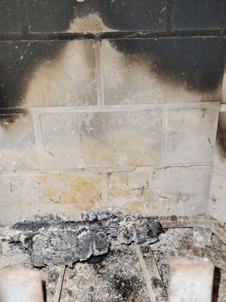 Image showing soot-covered tiles with hairline cracks above charred wood in a fireplace