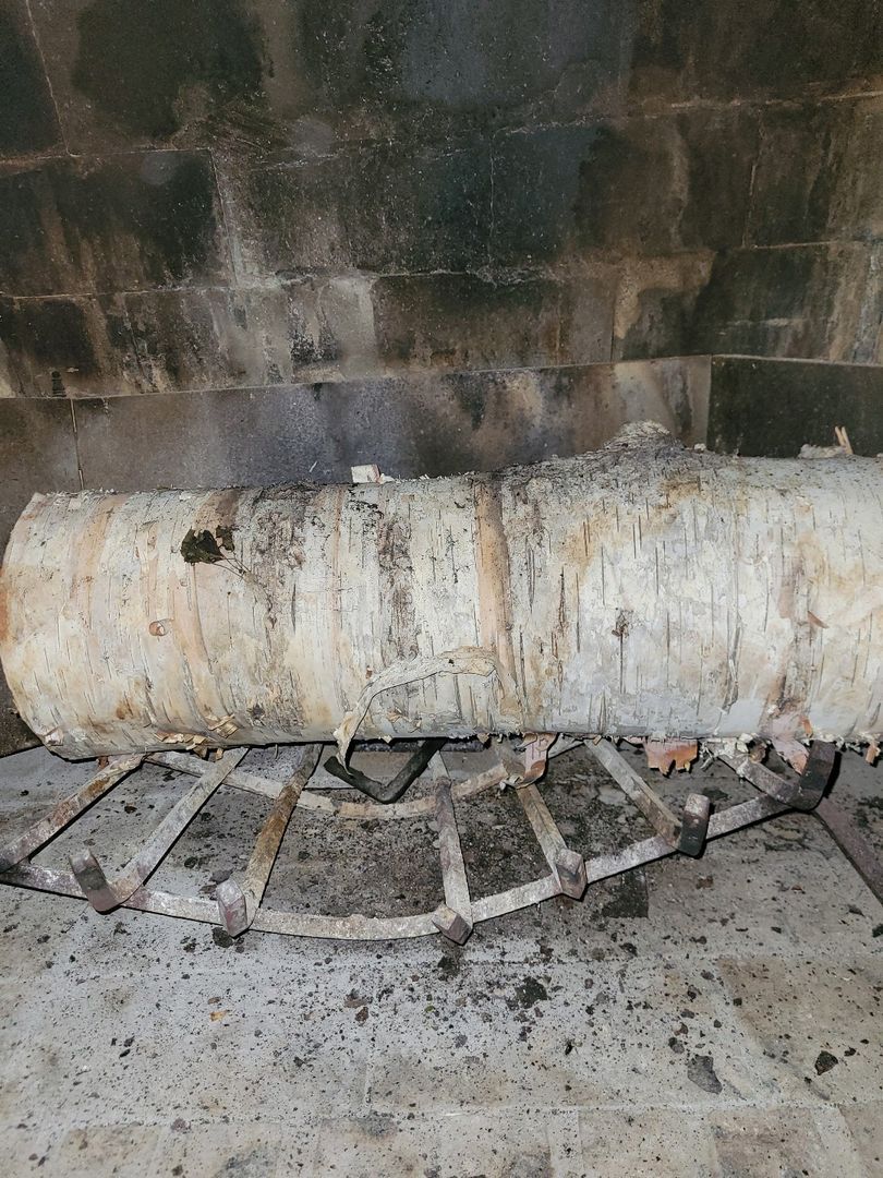 A birch log placed on a metal grate inside a fireplace with visible soot and ash