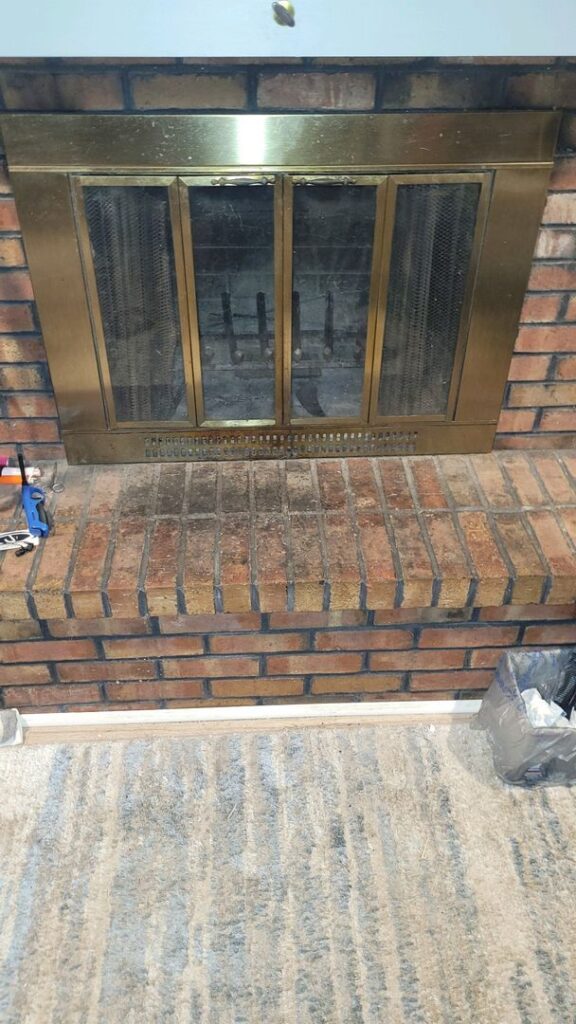 Brass fireplace doors set in a brick surround with maintenance tools on the hearth