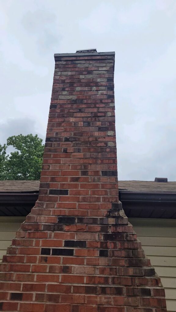Old red brick chimney with no smoke, extending into a cloudy sky above a house roof