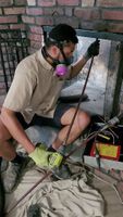 Technician wearing protective gear and using a drill to clean inside a brick fireplace