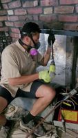 Technician wearing protective gear while working on chimney maintenance inside a home.